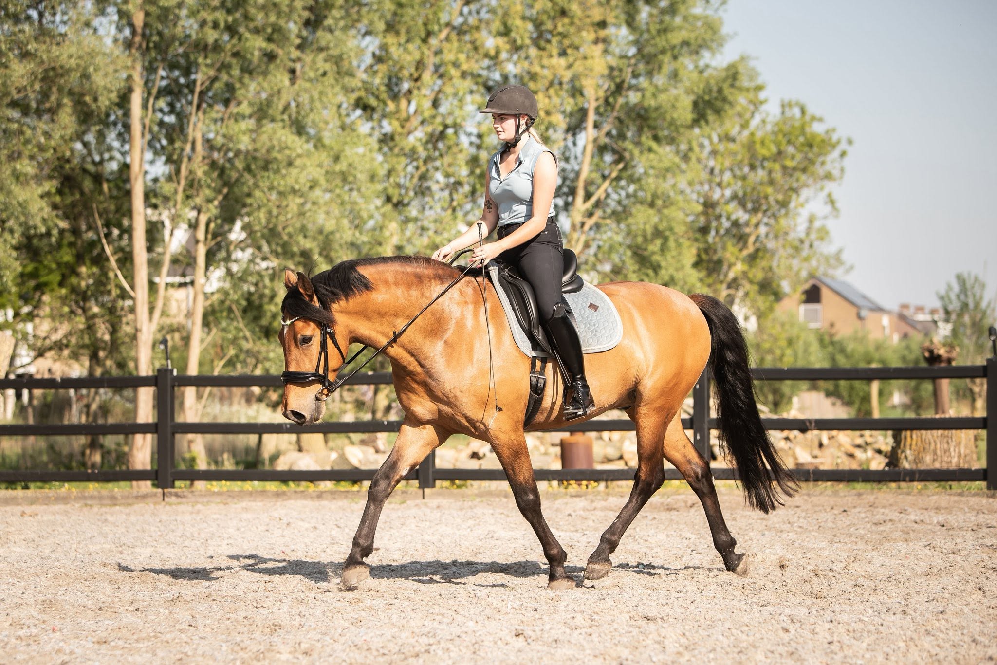 Susan rijdt haar bruine paard ontspannen in een zonnige buitenbak
